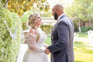 Smiling bride and groom facing each other holding hands